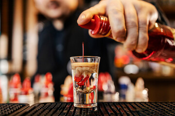 Close up of cocktail master adding alcohol into cocktail shot.