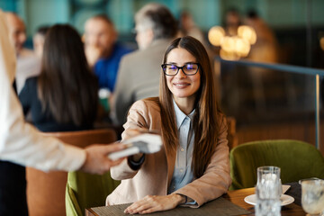 Smiling elegant lady paying her bill in cafe with m-banking app on pos device.