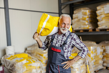 Portrait of senior industry worker carrying paper sack on shoulder in facility.