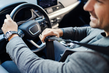 Naklejka premium Cropped picture of a businessman putting on his seat belt in a car.