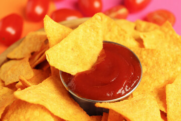Tasty ketchup and nachos on color background, closeup