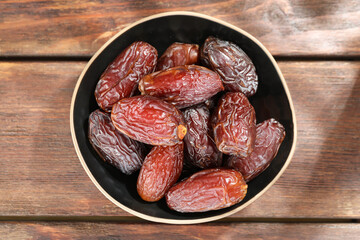 Many tasty dried dates in bowl on wooden table, top view