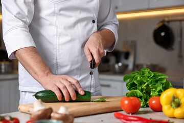 Professional chef cutting zucchini at table in kitchen, closeup