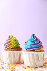 Delicious cupcakes with colorful cream and sprinkles on white wooden table against violet background, closeup. Space for text