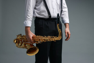 Professional musician with saxophone on grey background, closeup
