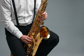 Naklejka premium Professional musician playing saxophone on grey background, closeup. Space for text