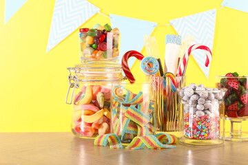 Candy bar. Many different sweets on wooden table against yellow background
