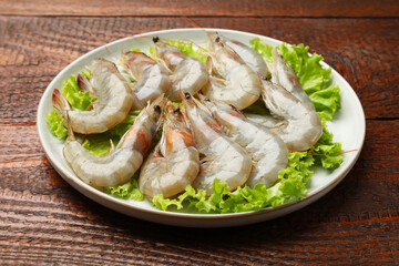 Fresh raw shrimps and lettuce on wooden table, closeup