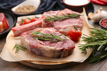 Pieces of raw beef, rosemary and tomatoes on wooden table, closeup