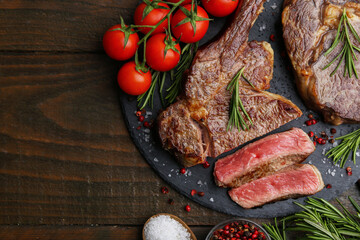 Pieces of delicious beef meat, spices and tomatoes on wooden table, flat lay. Space for text