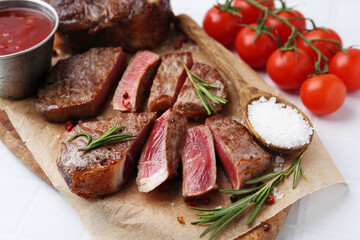 Pieces of delicious beef meat, spices and tomatoes on white table, closeup