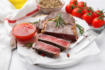 Pieces of delicious beef meat, spices, tomatoes and fork on white table, closeup