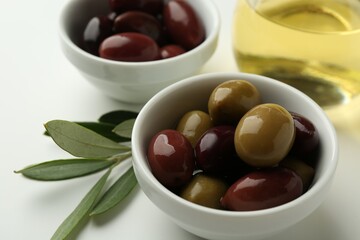 Tasty marinated olives, leaves and oil on white table, closeup