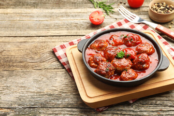 Delicious meatballs with tomato sauce in baking dish and spices on wooden table, closeup. Space for text
