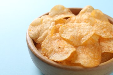 Tasty potato chips in bowl on light blue background, closeup