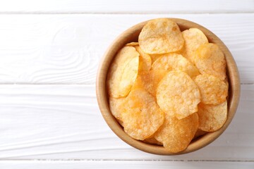 Tasty potato chips in bowl on white wooden table, top view. Space for text