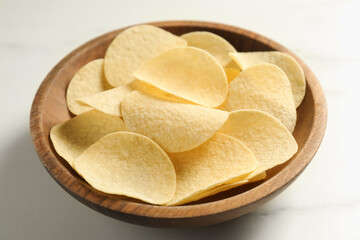 Tasty potato chips in bowl on white marble table, closeup