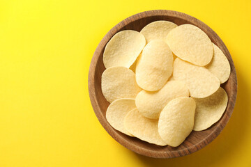 Tasty potato chips in bowl on yellow background, top view. Space for text