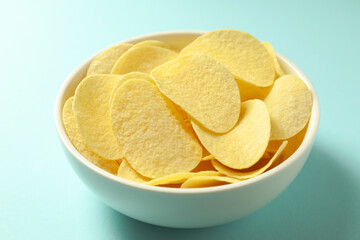 Tasty potato chips in bowl on light blue background, closeup