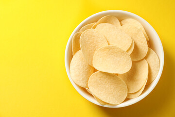 Tasty potato chips in bowl on yellow background, top view. Space for text