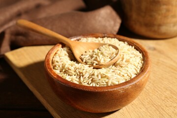 Brown rice and spoon in bowl on wooden table, closeup