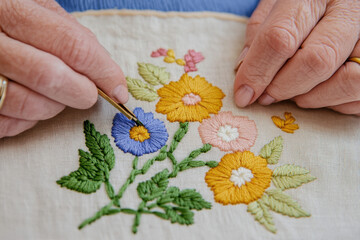 Isolated image featuring hands delicately embroidering vibrant flowers on fabric with a transparent background.