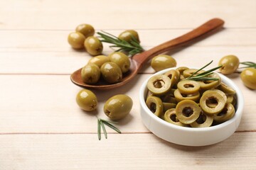 Delicious marinated olive rings, spoon with whole ones and rosemary on light wooden table, closeup. Space for text