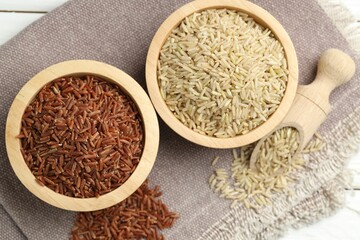 Different types of brown rice in bowls and scoop on table, flat lay