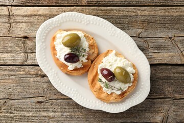 Delicious sandwiches with marinated olives, cream cheese and thyme on wooden table, top view