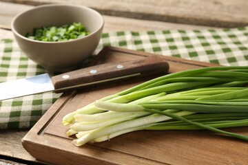 Fresh green onions and knife on wooden table, closeup