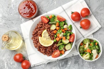 Delicious brown rice with vegetables and lemon slices served on grey textured table, flat lay