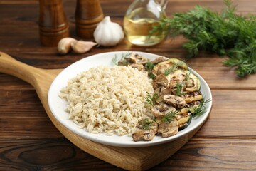 Delicious brown rice with mushrooms and dill served on wooden table, closeup