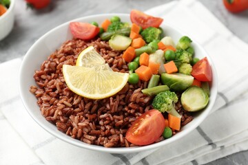 Delicious brown rice with vegetables and lemon slices served on grey table, closeup