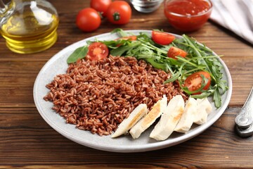 Delicious brown rice with chicken and salad served on wooden table, closeup