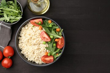 Delicious brown rice with vegetables on black wooden table, flat lay. Space for text