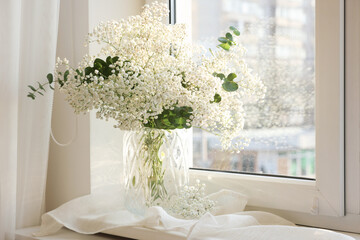 Bouquet of beautiful gypsophila flowers and eucalyptus branches in vase on window sill indoors