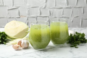 Healthy parsley smoothie in glasses, garlic, cabbage and leaves on white marble table against grey...