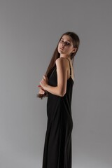 Fototapeta premium Elegant woman posing in a sleek black dress against a neutral backdrop in a studio setting