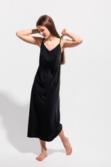Model showcases elegant black dress in minimalistic studio setting during daylight hours