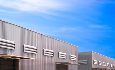 2 factory warehouse industrial buildings with ventilation louvers on gray aluminium corrugated metal wall against blue sky background, low angle and perspective side view with copy space