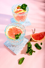 Chilled cocktail with grapefruit slices and fresh mint leaves on pink background. Summer refreshing drinks. Citrus soda