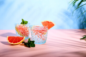 Chilled cocktail with grapefruit slices and fresh mint leaves on pink background. Summer refreshing drinks. Citrus soda