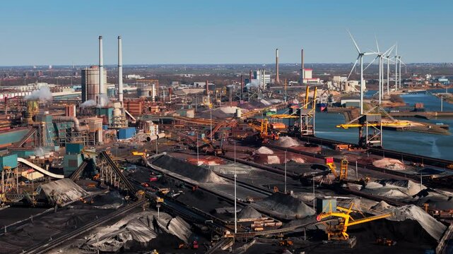 Industrial steel plant in IJmuiden, Netherlands, with large chimneys, conveyor belts, and emissions. Aerial view of a major production hub, showing both traditional and renewable energy elements.