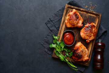 Roasted chicken thighs with ketchup on a rustic wooden board. Top view with copy space.