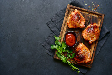 Roasted chicken thighs with ketchup on a rustic wooden board. Top view with copy space.