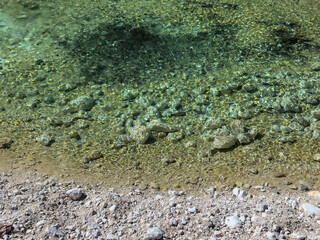clear turquoise river water over a rocky shoreline. bright sunlight, sparkling reflections on water surface, stone texture, stone background. assorted