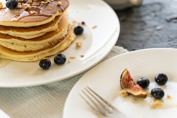 Pancakes stacked with figs and blueberries on a white plate on a light gray background.