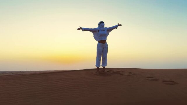 Stylish woman rotate standing on a sandy desert horizon at sunset with arms outstretched
