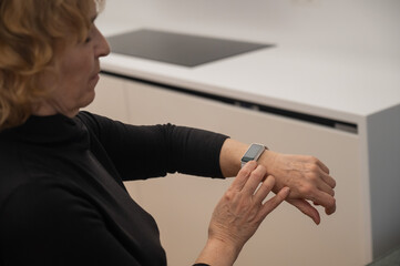 Obraz premium Elderly Caucasian woman looking at smart watch. Close-up of hands. 
