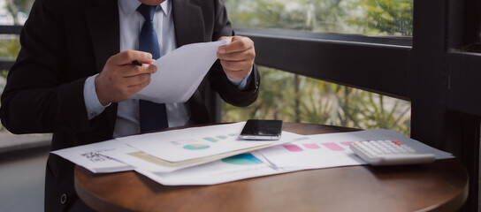 Businessman analyzing financial documents with a calculator and smartphone. Concept of finance,...